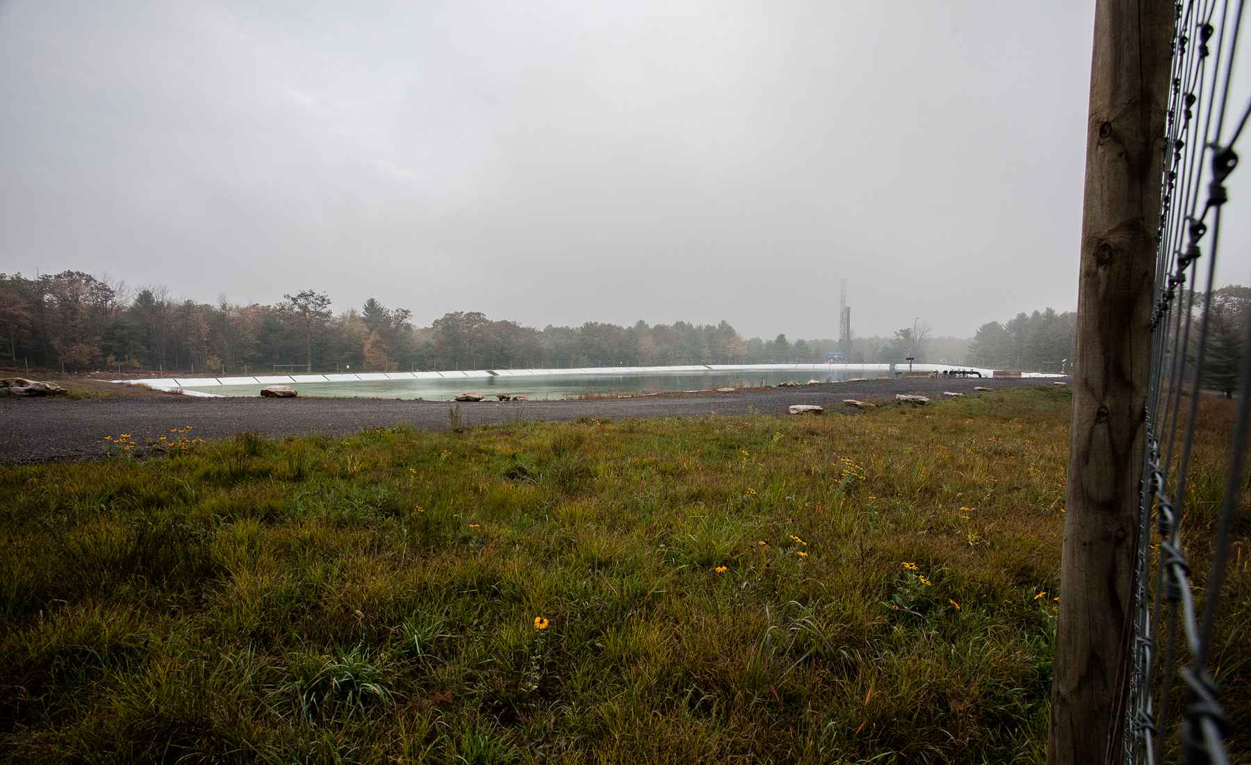 A water impoundment pond containing fresh water. In the distance is an active drill rig and work site (photo: Chad Shmukler). fracking water impoundment pond